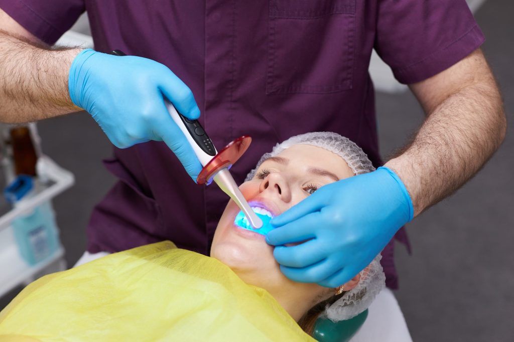 Dentist applying fluoride treatment with curing light to patient’s teeth