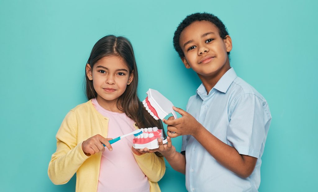 Two children demonstrating how to brush teeth using a dental model