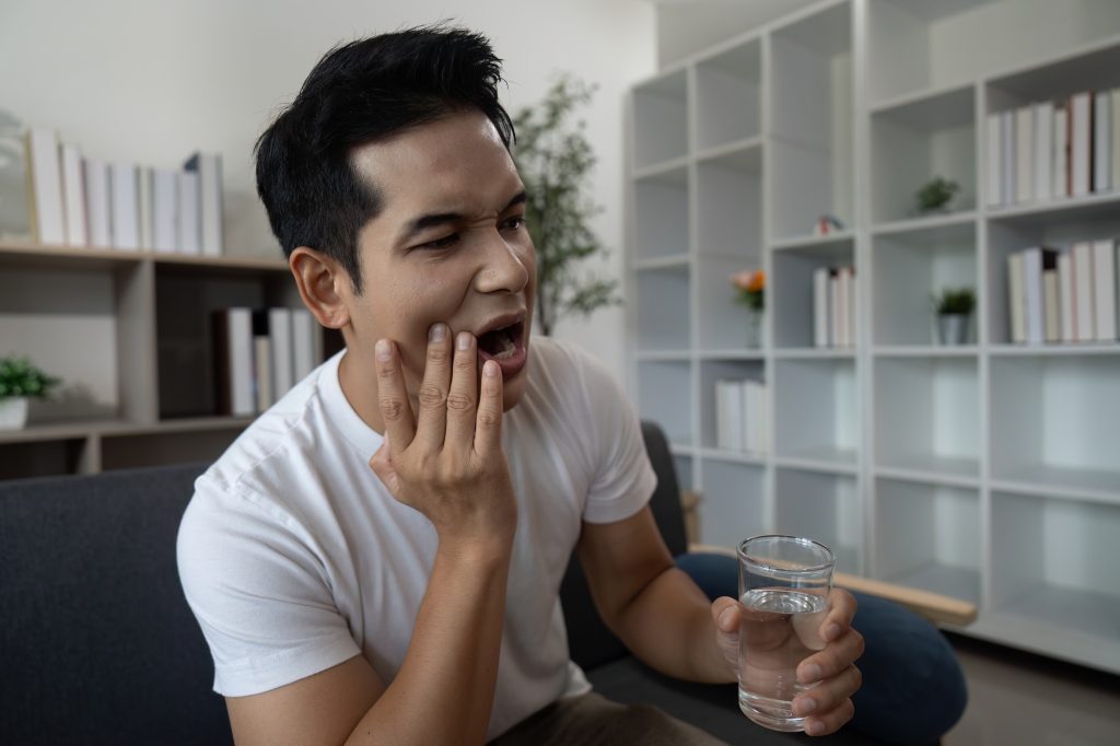 Person experiencing tooth sensitivity while drinking a cold beverage